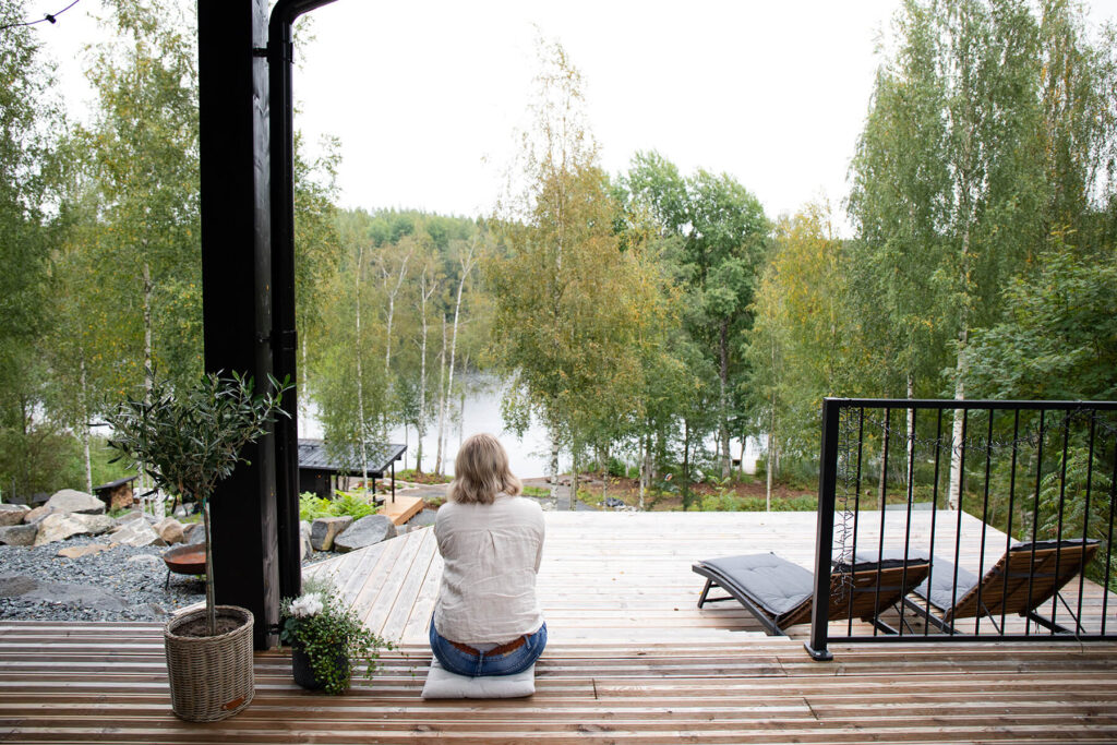 Nainen ihailemassa järvimaisemaa modernin hirsihuvilan terassilla